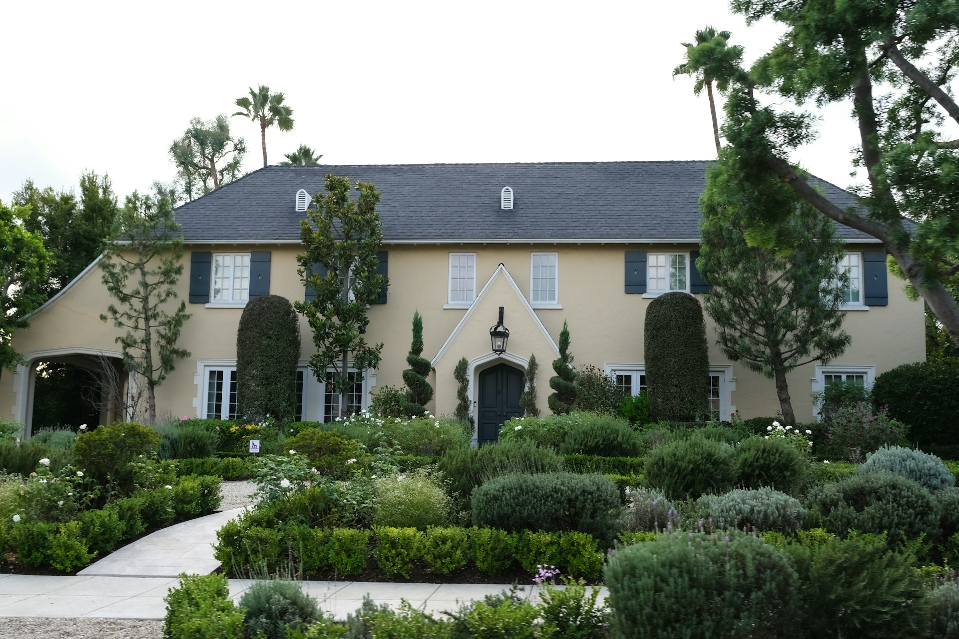 A large tan house with manicured gardens and palm trees.